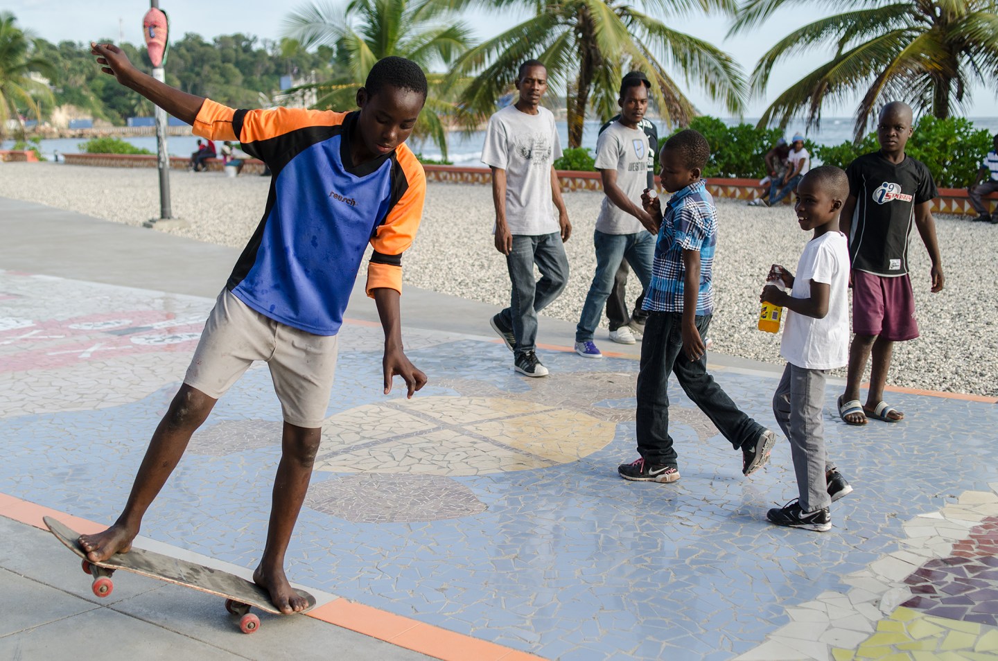 A young boy skateboards on a colorful pavement while other children observe nearby