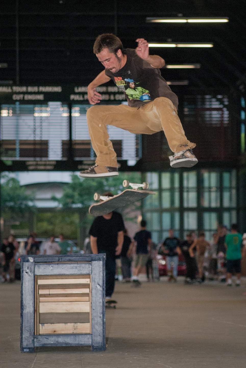Skateboarder performing a trick above a wooden obstacle in an indoor skate park