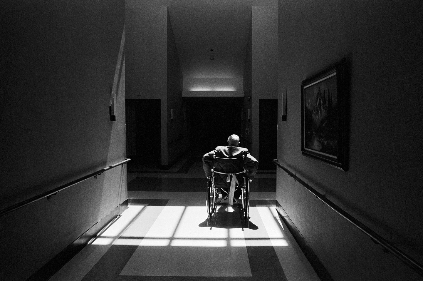 A person in a wheelchair sitting in a dimly lit corridor with light streaming through