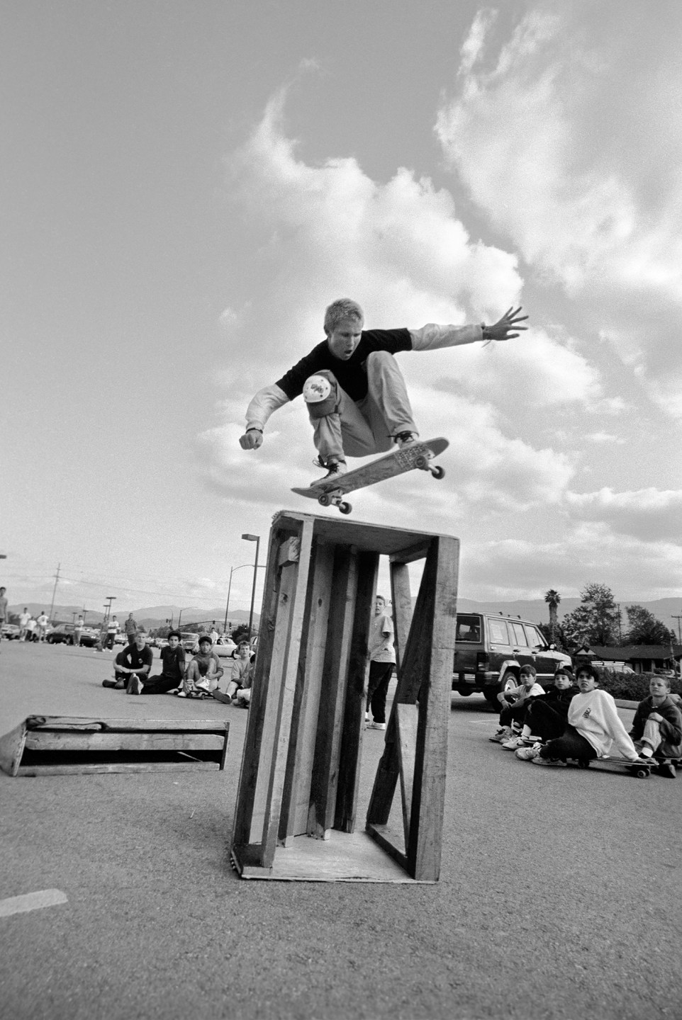 Skateboarder performing a trick over a wooden obstacle with spectators watching