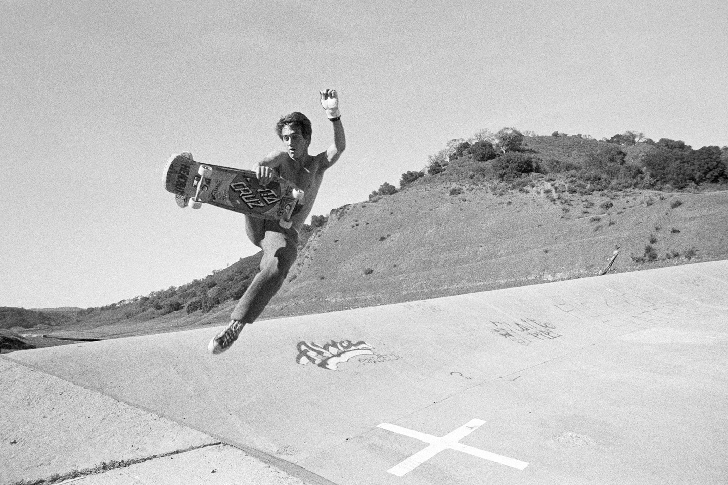Skateboarder performing an airborne trick over a concrete barrier in a rural setting