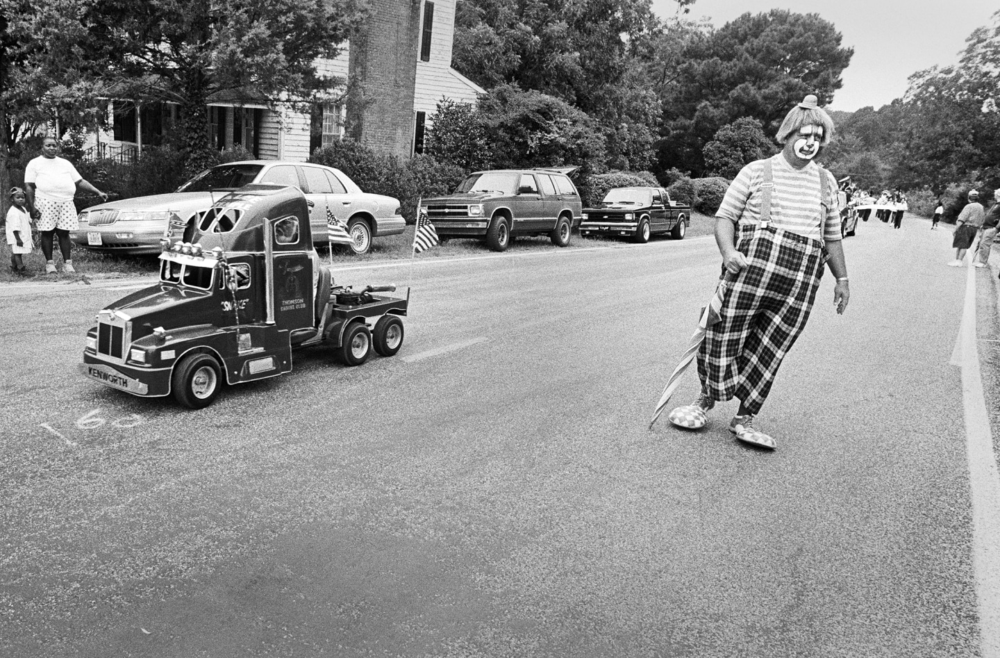 A clown walking alongside a toy truck in a parade setting