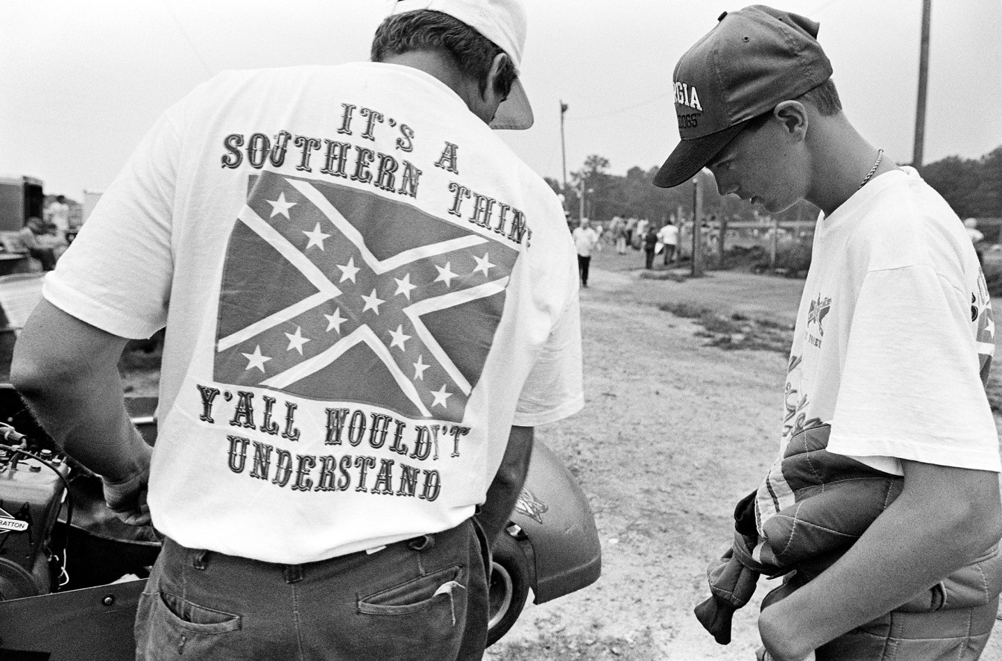 Two boys examine a car, one wearing a T-shirt with a Confederate flag and text that reads "It's a Southern Thing, Y'all Wouldn't Understand."