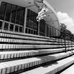 Skateboarder performing an ollie over stairs in a black and white photo.