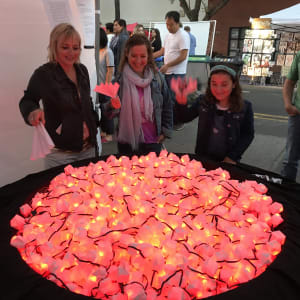 Three people interact with a glowing installation of pink and red lights at an outdoor event