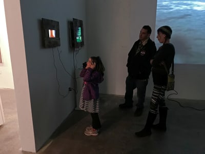 A young girl explores an interactive art installation while two adults observe nearby