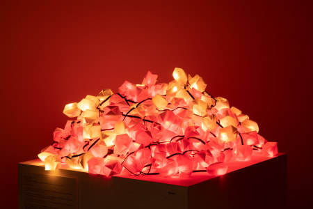 A pile of glowing pink and yellow decorative lights on a light surface against a red background