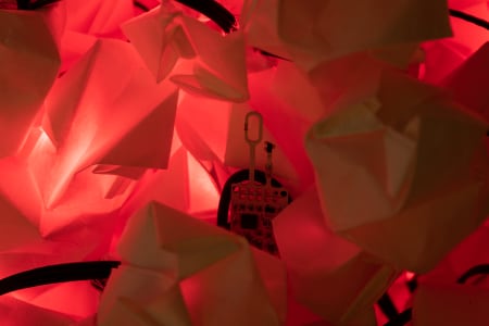 A small electronic device is nestled among crumpled white paper illuminated by a red light
