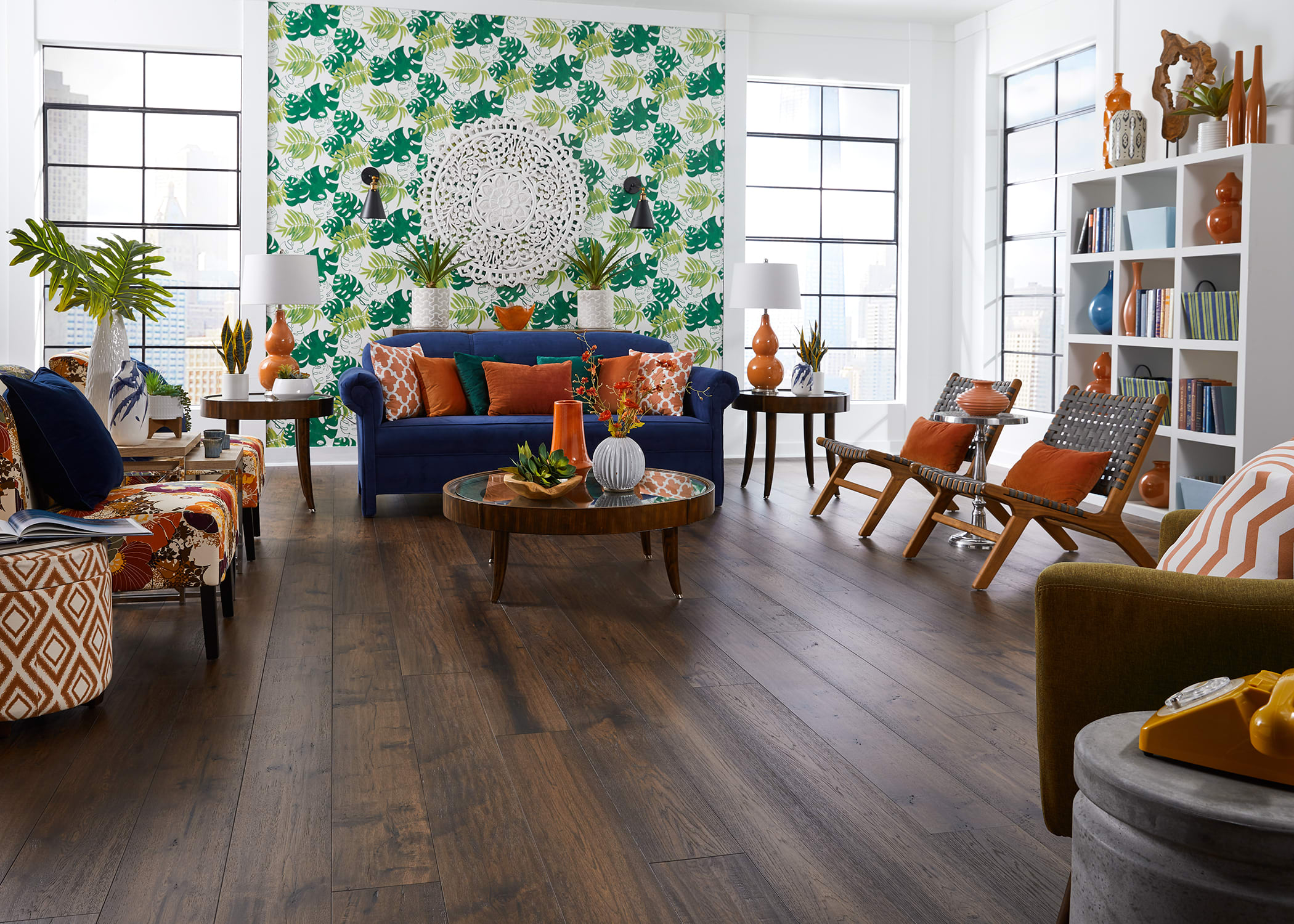 This beautiful living room features deep brown hickory flooring, blue couch, pops of orange and green, with a bright green print accent wall to balance the space.