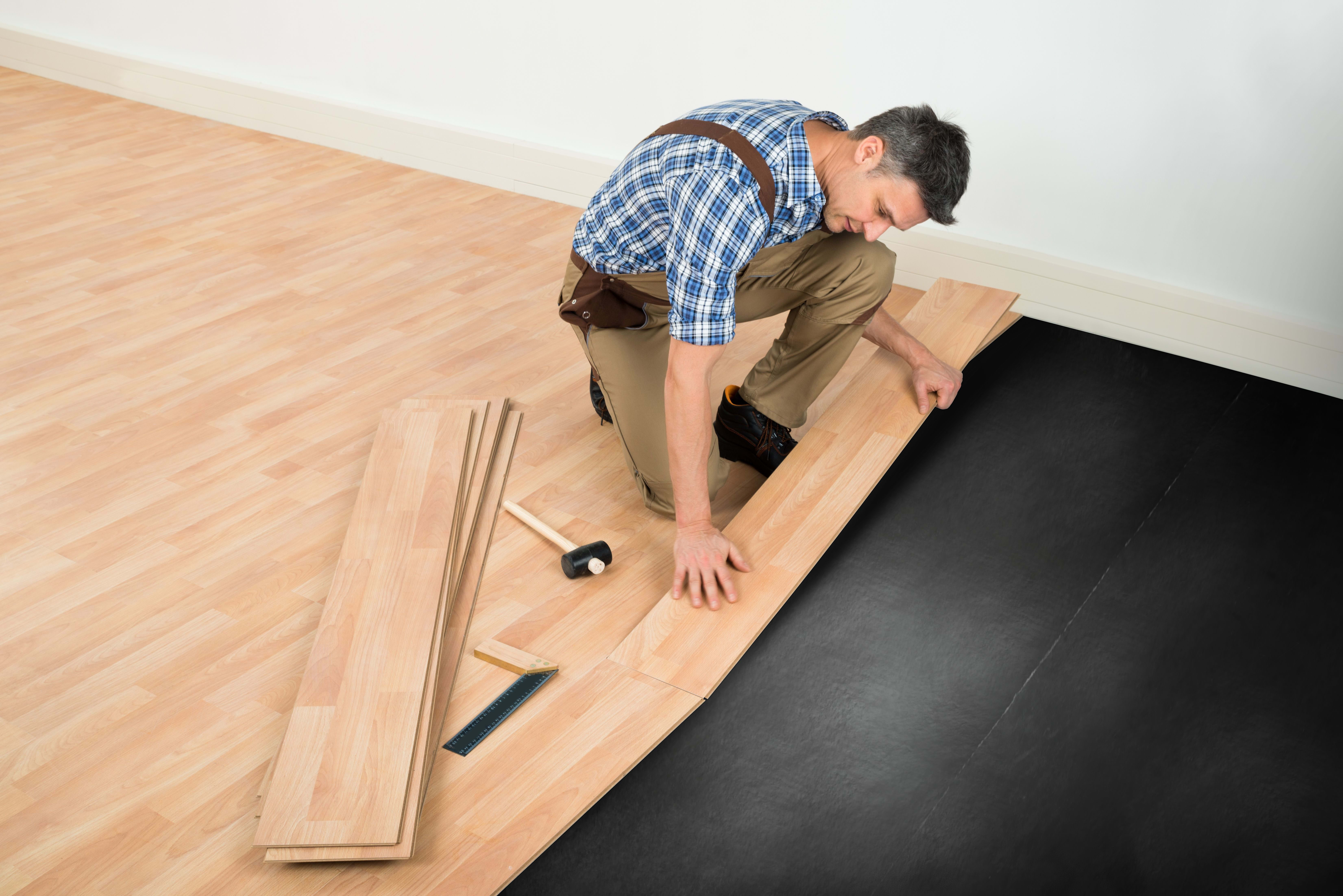 A man installs flooring over an underlayment he placed on the subfloor