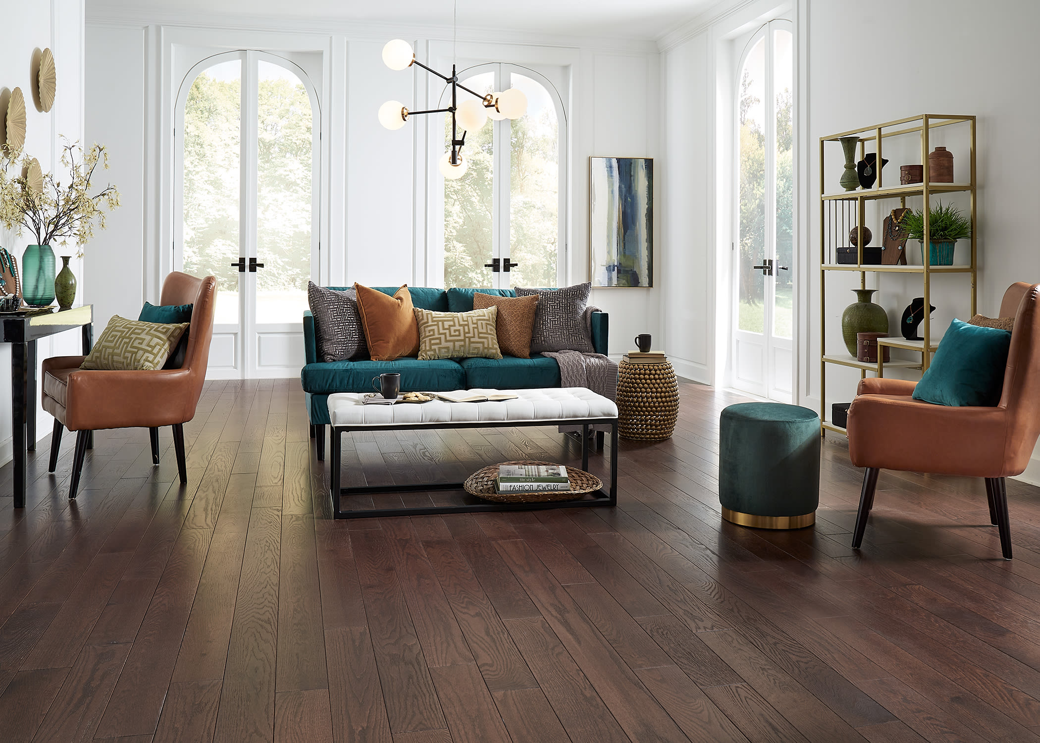 Tall arched double doors, tufted coffee table, modern candelabra, and lots of light in this sunroom are balanced by the rich planks of Bellawood Stratford Oak Distressed Solid Hardwood Flooring