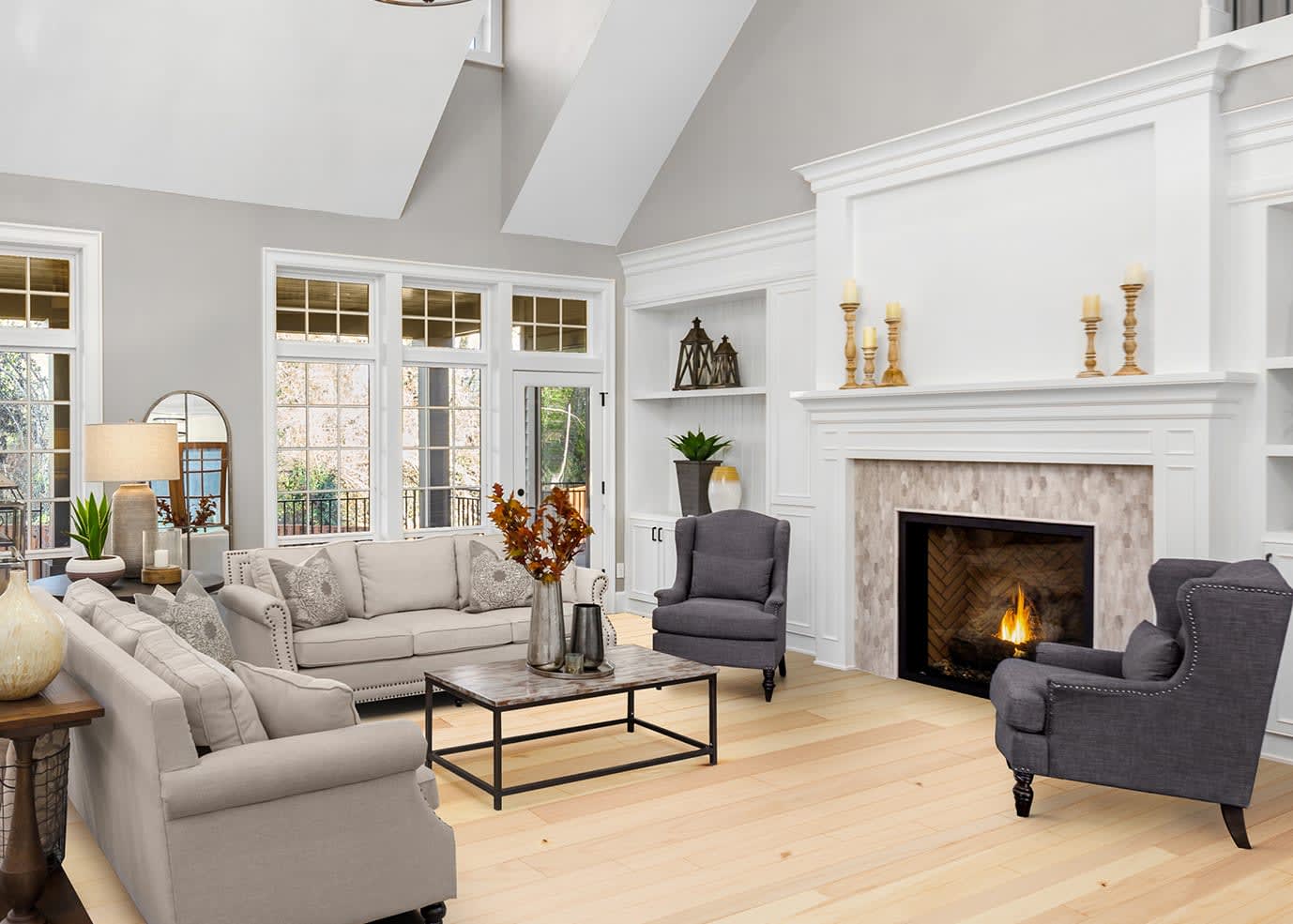 This living room features high ceilings, large windows, with a glowing fire in the fireplace, with Bellawood Select Maple hardwood flooring