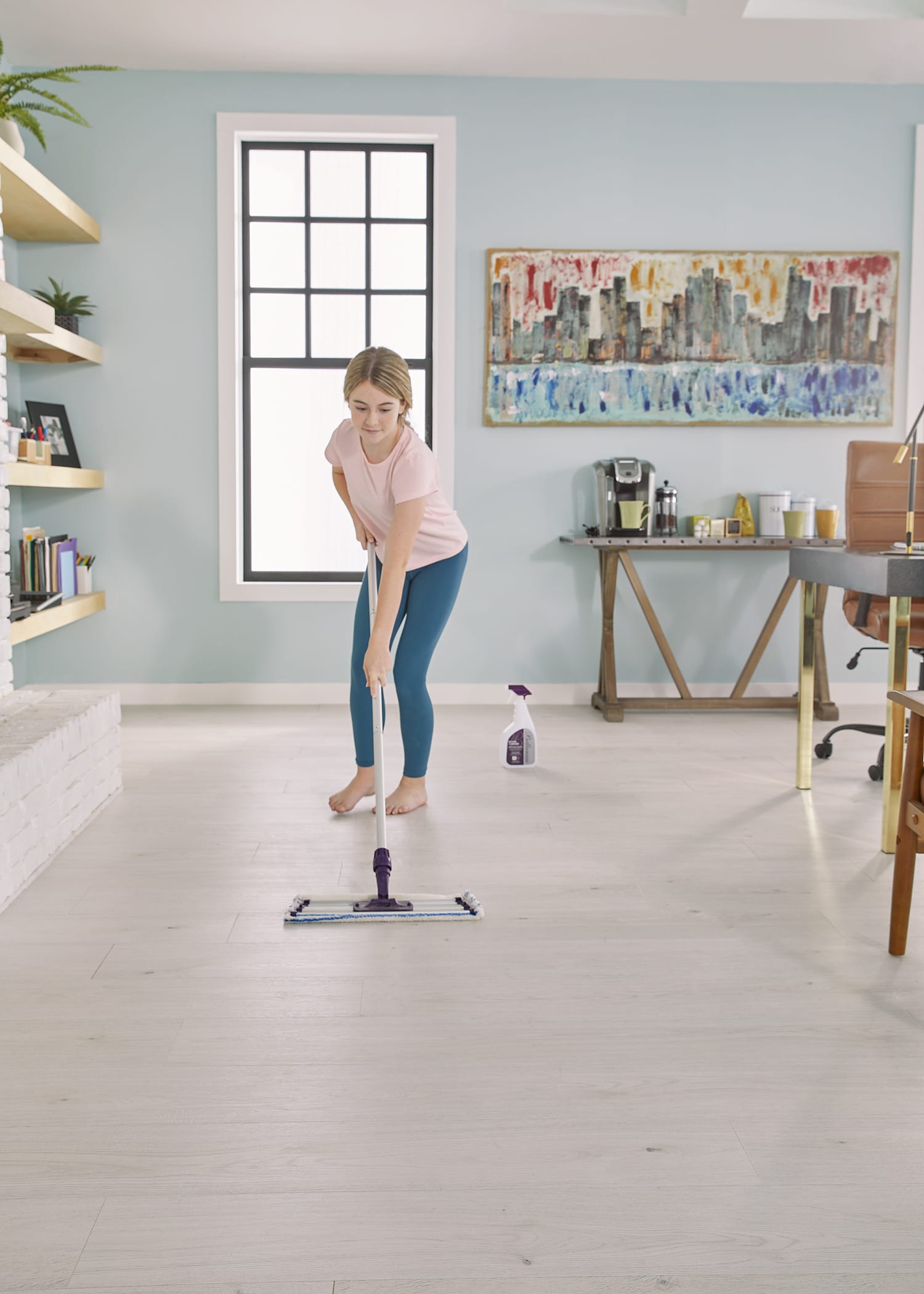 A child happily focuses on dry-mopping the floor of a bright fitness room/office for spring cleaning.