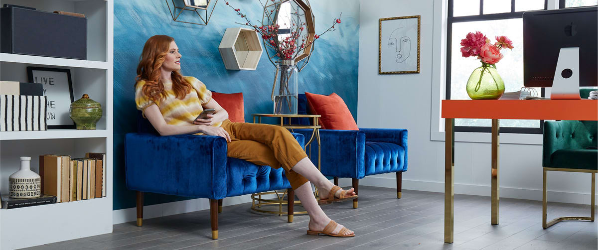 A Woman sits in a colorful, well designed room created with maximalist decor ideas.