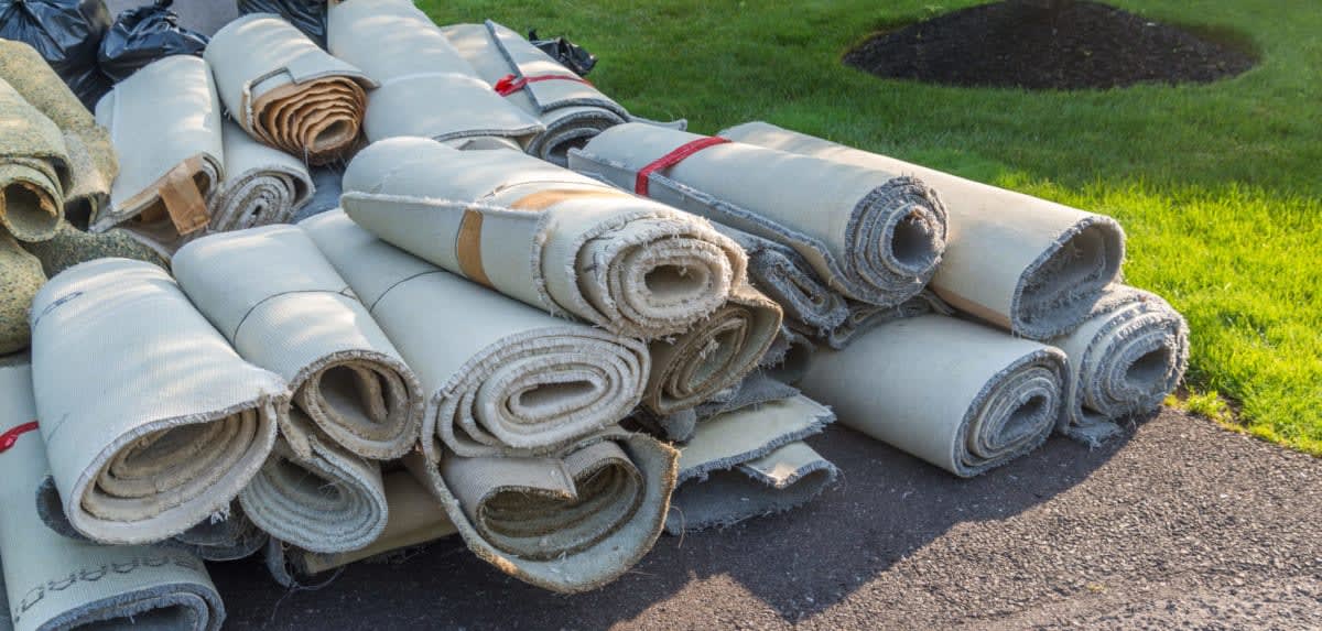 Rolls of carpet are stacked up and ready for removal in the driveway to get ready for a new floor. og:image