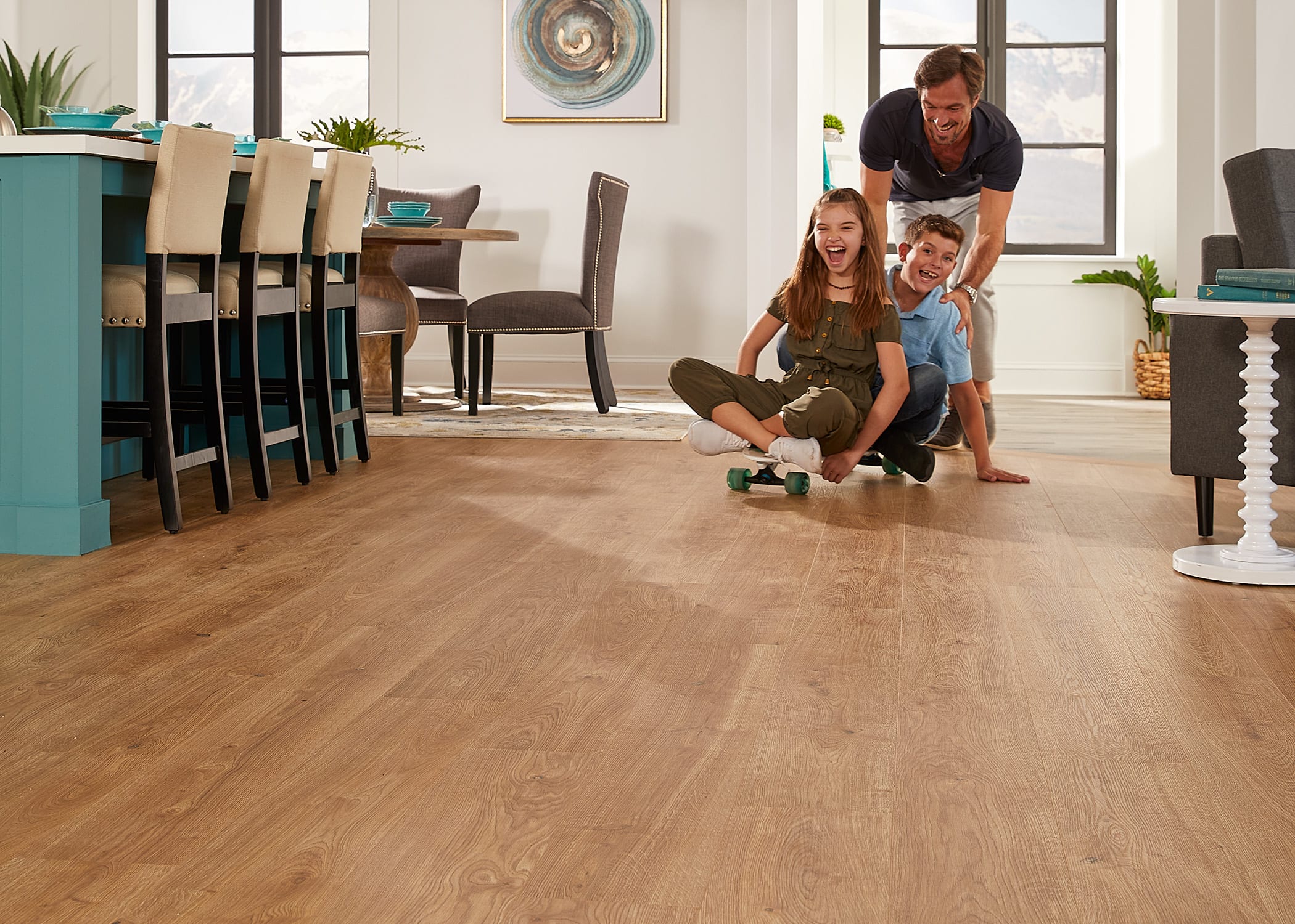 A family uses a skateboard on their new floor. Duravana Bay Bridge Oak Hybrid Resilient Flooring is a refined, timeless blond-wood flooring made to stand up to busy family lifestyles.