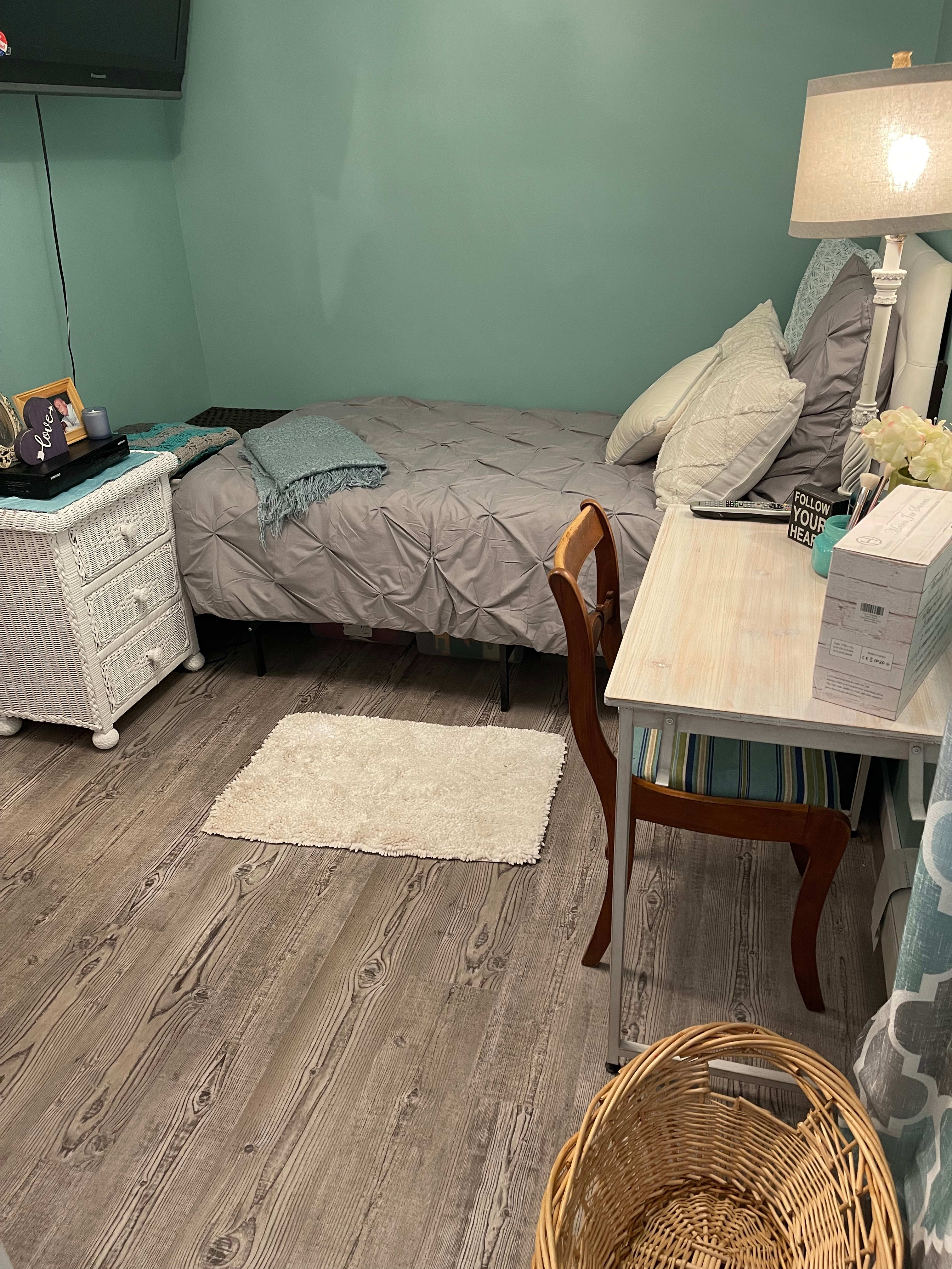 This bedroom shows the turquoise wall, cream color combinations, wicker textures, and Old Port Pine waterproof rigid vinyl plank flooring.