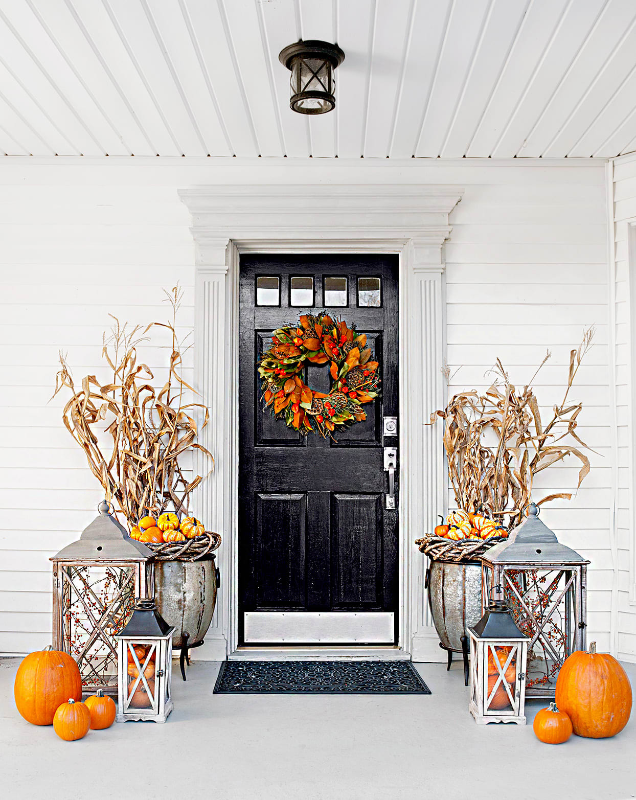 Porch with autumn wreath on the door, and decorated with bright orange pumpkins on each side.