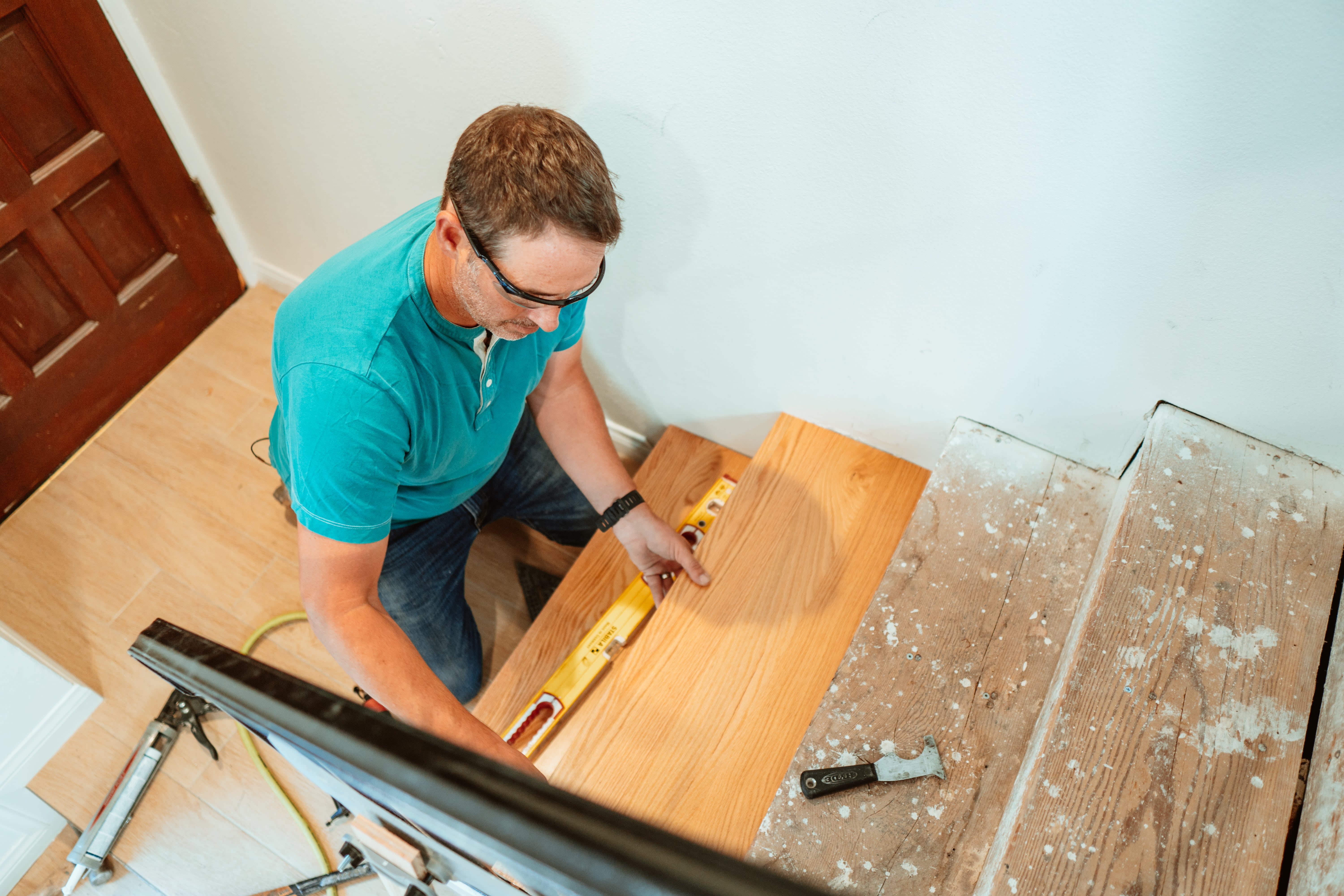 Contractor Josh Temple of HGTV wearing a turquoise shirt as he crouches in a stairwell fitting new hardwood tread into place.