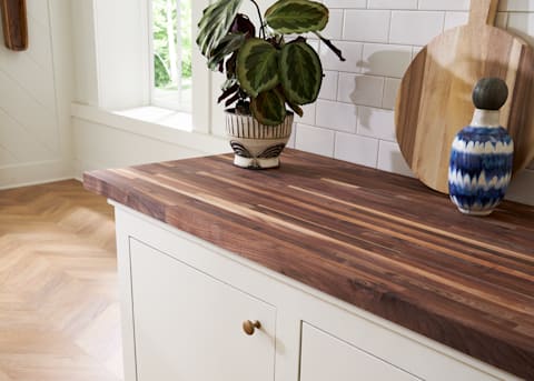 Unfinished American Walnut 12 ft. Length x 25 in. Wide x 1-1/2 in. Thick Butcher Block Countertop on countertop in kitchen with subway tile on wall and round cutting board against wall