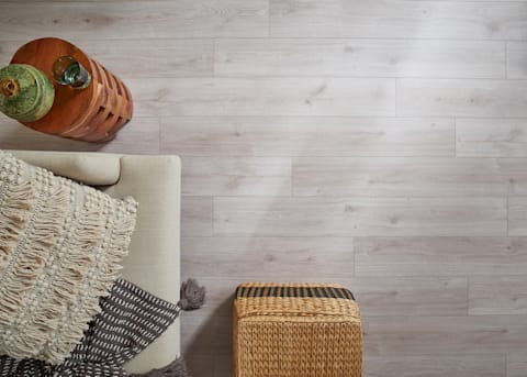 5mm+Pad Ravello Oak Rigid Vinyl Plank Flooring close up of floor with beige armchair and rattan ottoman