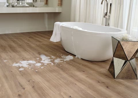 7mm+Pad Lake Worth Oak Hybrid Resilient Flooring closeup of floor with spill on it and oval freestanding bathtub