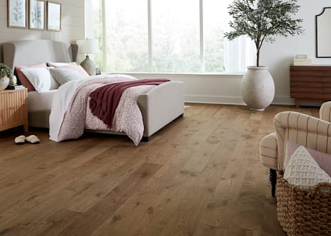 5/8 in. x 7.5 in. Monaco White Oak Engineered Hardwood Flooring in bedroom with beige upholstered bed plus large clay pot with decorative tree and striped upholstered chair