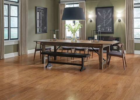 3/8" x 5 in. Butterscotch Oak Engineered Hardwood Flooring in dining room with dark green walls plus medium brown wood dining table and chairs with black drum shade pendant light over table and black and white artwork on walls