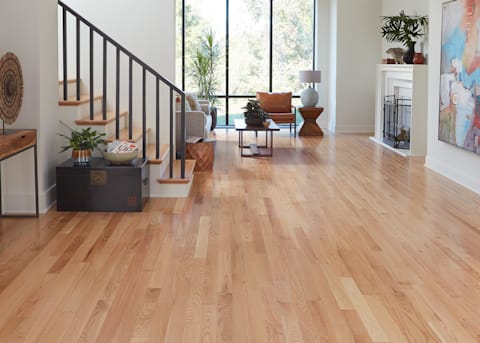 3/4 in. x 3.25 in. Red Oak Solid Hardwood Flooring in lower level family room with white fireplace and brown leather chair next to beige sofa