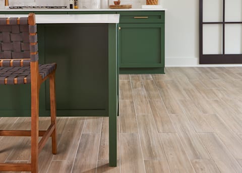 36 in. x 6 in. Cottage Wood Ash Porcelain Tile in kitchen with green cabinets white counters and wood island stools