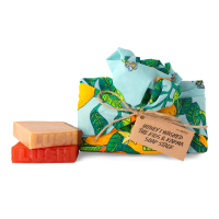 Honey I Washed The Kids And Karma Soap Stack A colourful tengri wrap with an orange and leaves design and a brown tag with black text. Next to the wrap is a brown soap stacked on top of an orange, square piece of soap