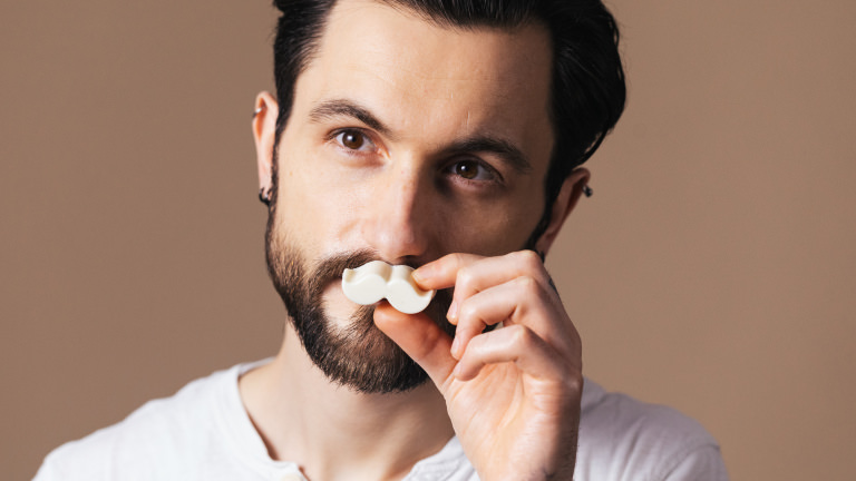 Dirty Beard Oil moustache shaped naked facial oil being held to models face