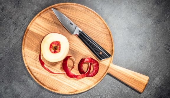 A VEGA paring knife on a wooden board next to a peeled apple
