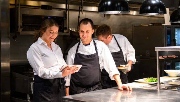 Zwei Personen in einer Gastronomieküche schauen zusammen auf ein Tablet.