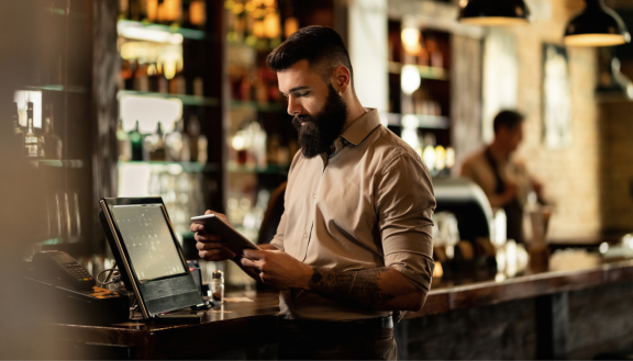 Ein Mann steht hinter dem Tresen an der Kasse und schaut auf ein Tablet.