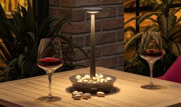 Schwarze Tischlampe von Sompex in einem Restaurant neben 2 Weingläsern auf einem Holztisch platziert