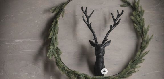 An der Wand befestigter schwarzer Hirschkopf aus Aluminium, umringt von einem Kranz aus Tannenzweigen.
