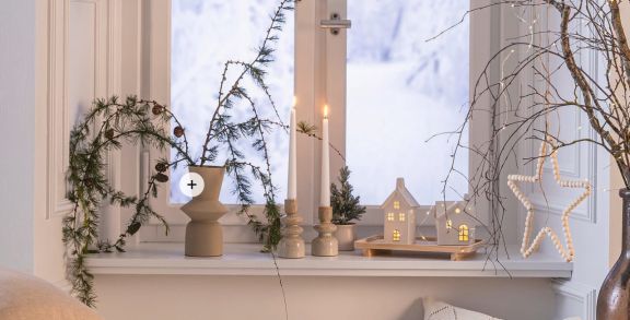 Weihnachtlich dekorierte Fensterbank mit Stielkerzen und Lichthäusern.