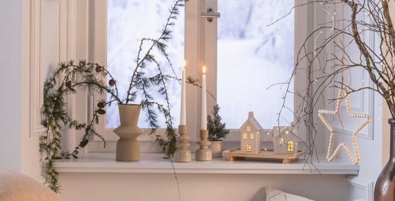 Weihnachtlich dekorierte Fensterbank mit Stielkerzen und Lichthäusern.