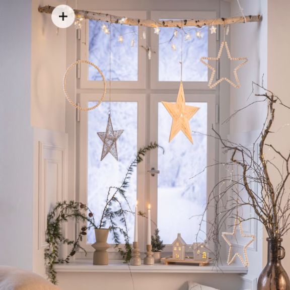 Weihnachtlich dekoriertes Fenster mit Lichterketten, Sternanhängern und Lichhäusern.