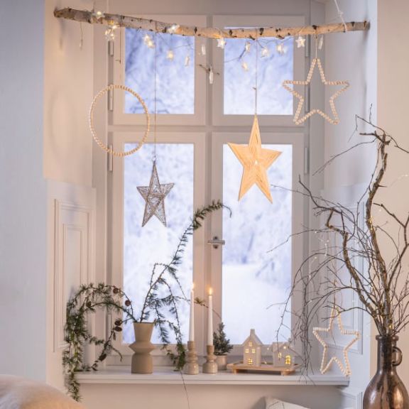 Weihnachtlich dekoriertes Fenster mit Lichterketten, Sternanhängern und Lichhäusern.