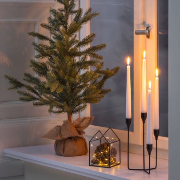 Fensterbank dekoriert mit einem kleinen Tannenbaum, einem Kerzenständer und einen kleines Glashäuschen mit Lichterkette.