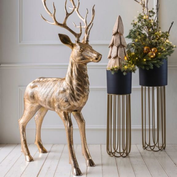 Großer Dekohirsch in gold, zwei Übertöpfe auf Ständern gefüllt mit kleinen Tannenbäumen.