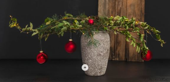 Verschiedene Baumzweige in einer Vase, geschmückt mit roten Weihnachtskugeln