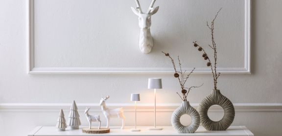 Weihnachtlich dekoriertes Sideboard im Eingang. Mit kleinen Tannenbaum- und Hirschfiguren, Tischlampen und Vasen mit Zweigen.