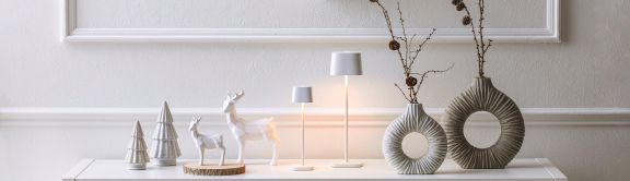 Weihnachtlich dekoriertes Sideboard im Eingang. Mit kleinen Tannenbaum- und Hirschfiguren, Tischlampen und Vasen mit Zweigen.