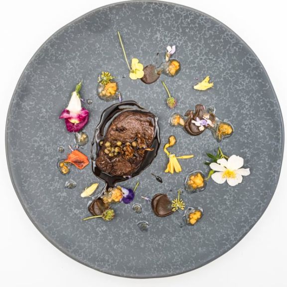 Hirschrücken mit grünen Holunderbeeren und getrockneten Pilzen dekoriert mit Blüten.