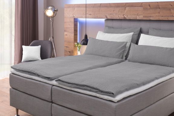 schlichtes Einbettzimmer mit hellgrauer Bettwäsche