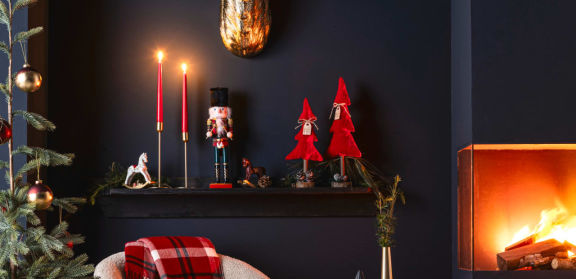 Weihnachtlich dekorierter Kaminsims mit Nussknacker, roten Tannenbaum-Figuren und roten Stabkerzen.