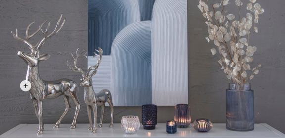 Sideboard dekoriert mir silbernen Hirschen, verschiedenen Teelichthaltern und einer Vase mit Dekogesteck. Alles ist in silber und blau gehalten.